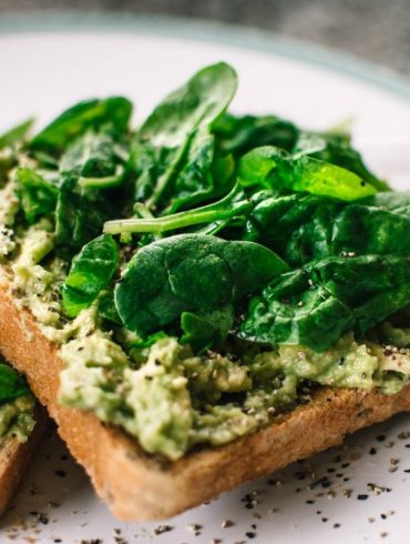 basil leaves and avocado on sliced bread on white ceramic plate