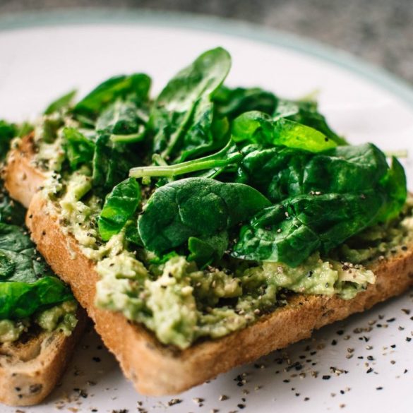 basil leaves and avocado on sliced bread on white ceramic plate